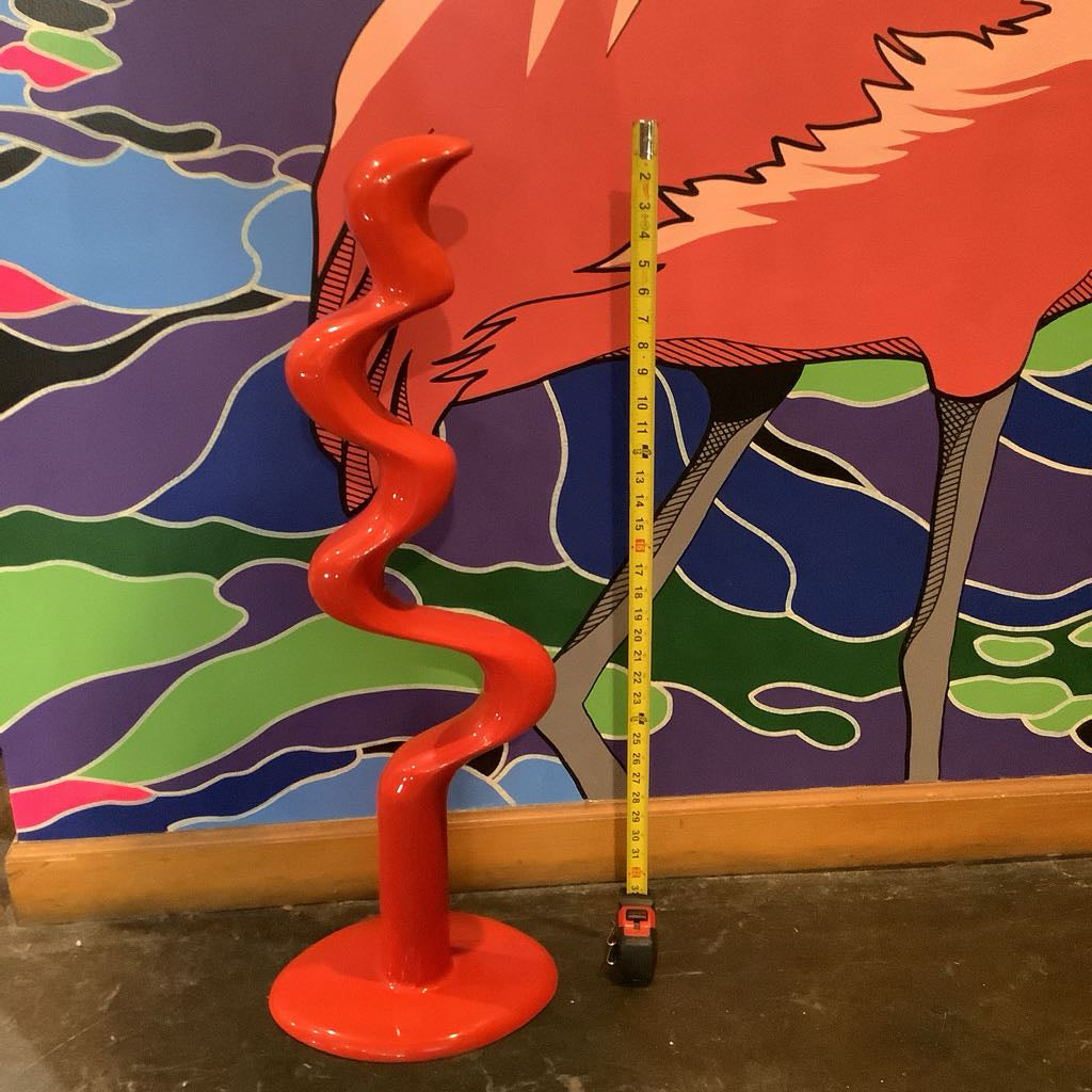 Red spiral object with a measuring tape against a colorful abstract wall.