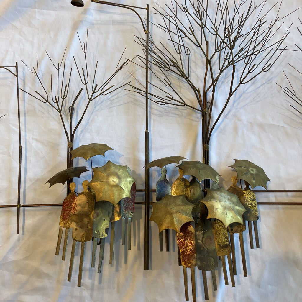 Metal wall art of people with umbrellas under trees on a textured white background