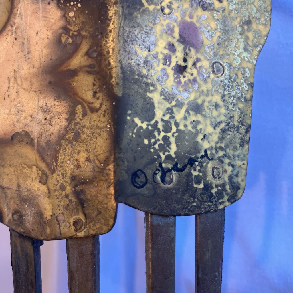 Metal object with artists signature on a white shadowed background