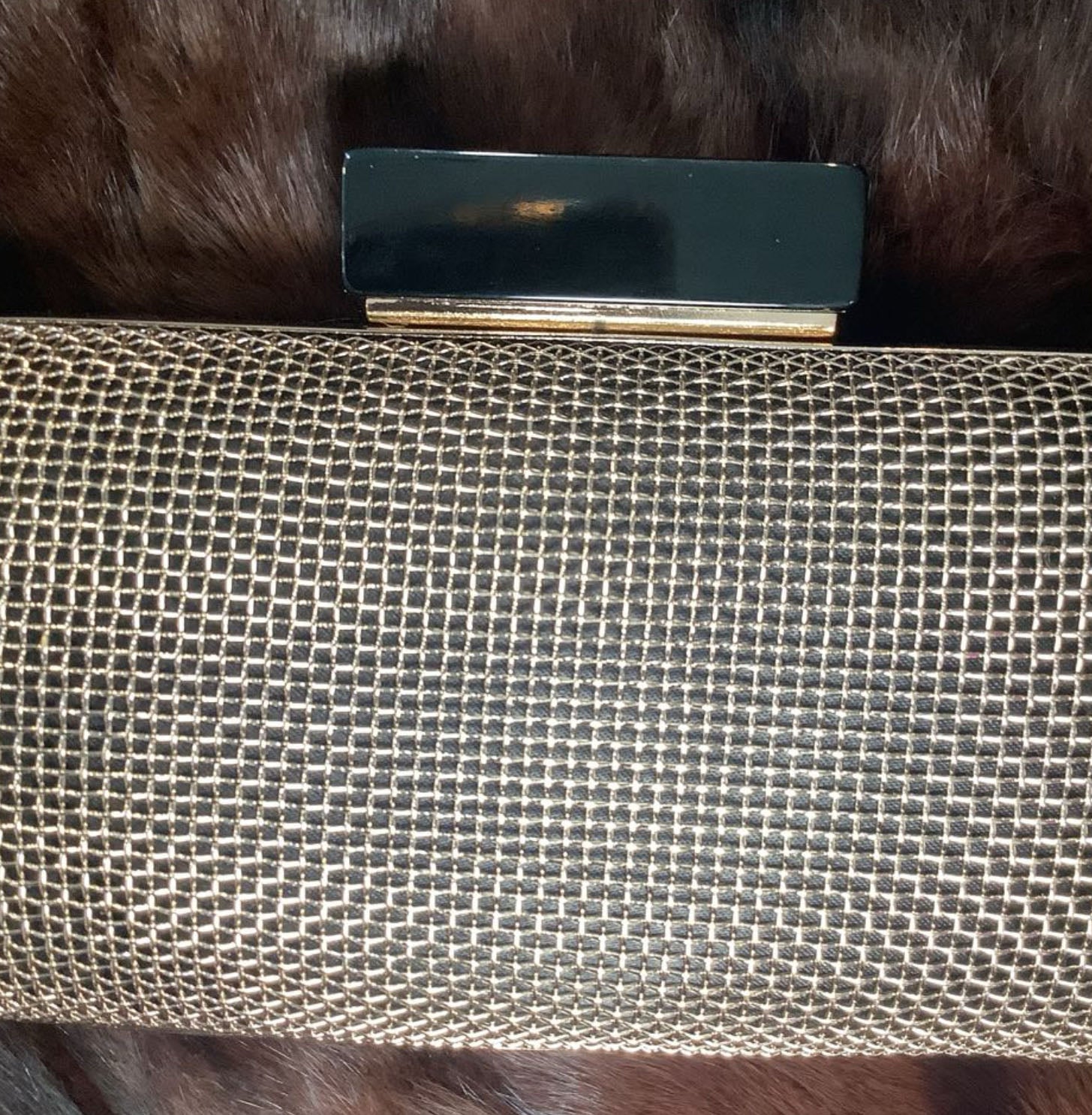 Close-up of a textured clutch bag with a metallic clasp on fur.