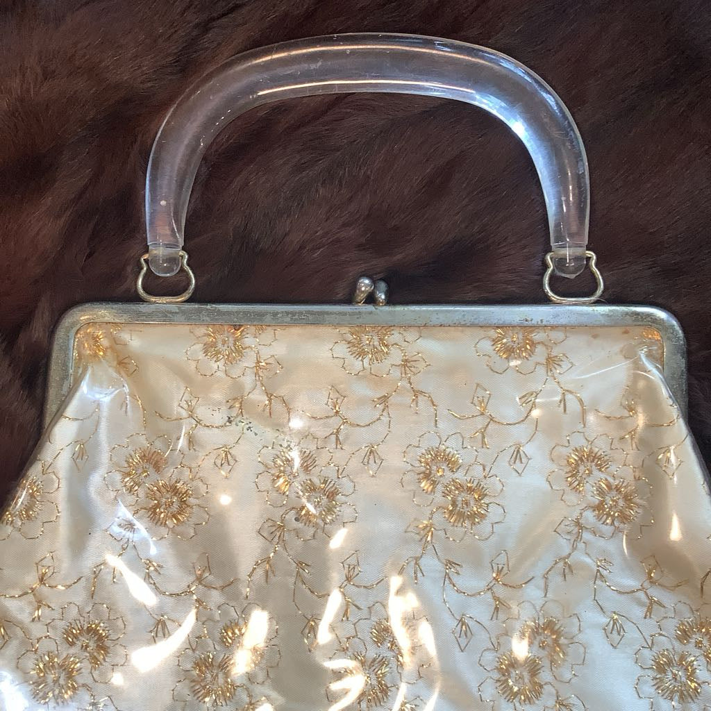 Vintage handbag with floral embroidery and clear handle on a textured brown background