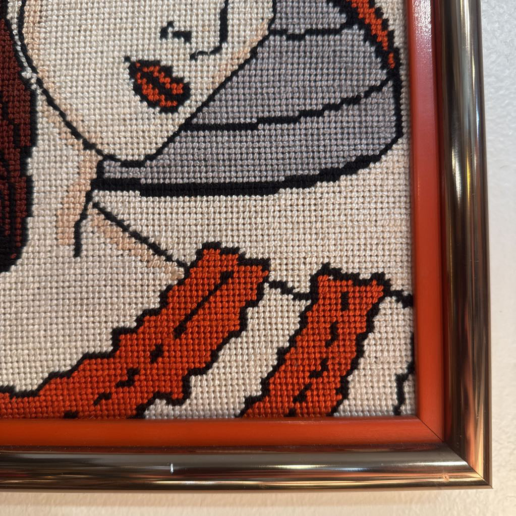 Framed cross-stitched picture of a ghost with a red ribbon on a white background