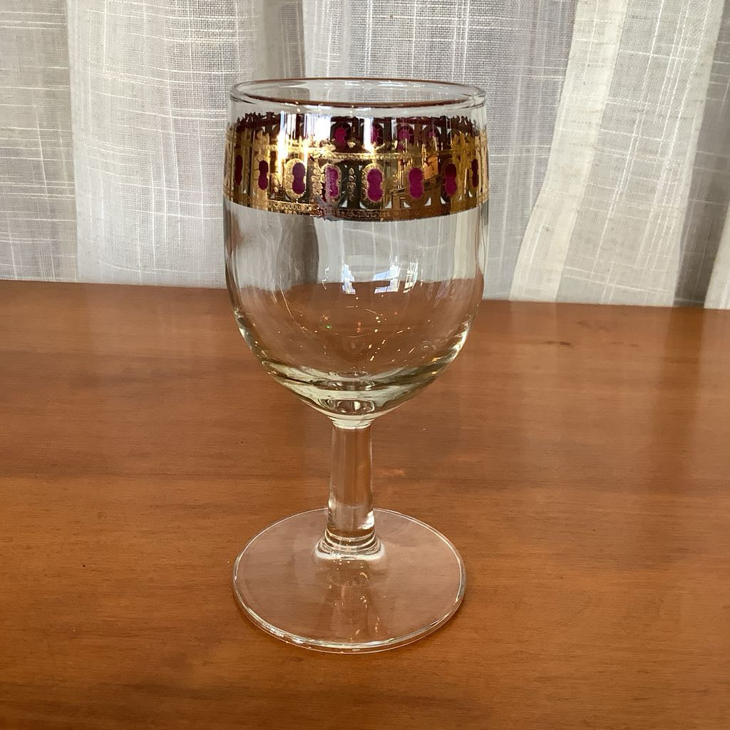 Clear glass with gold and red decorative band on a wooden surface