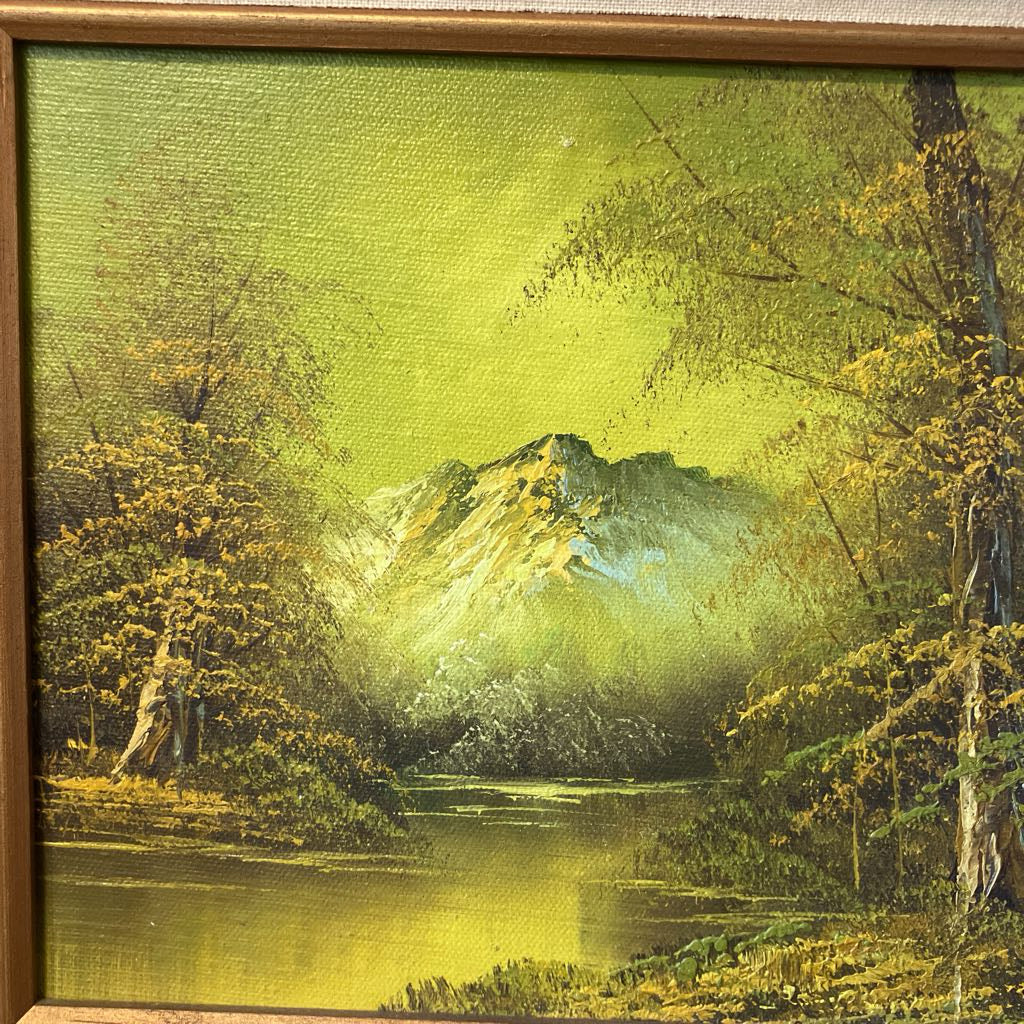 Framed painting of a mountain landscape with trees and a lake.