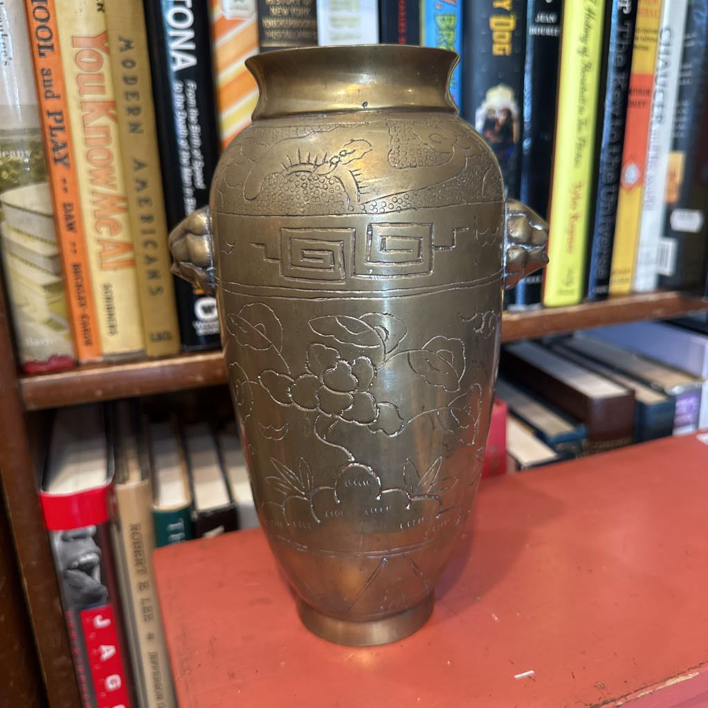 Bronze vase with intricate designs on a bookshelf