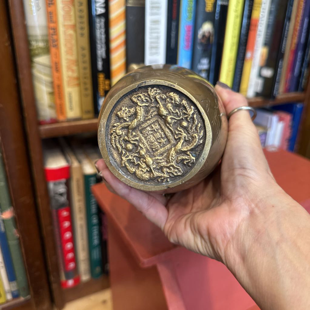 Hand holding a decorative brass object in front of a bookshelf