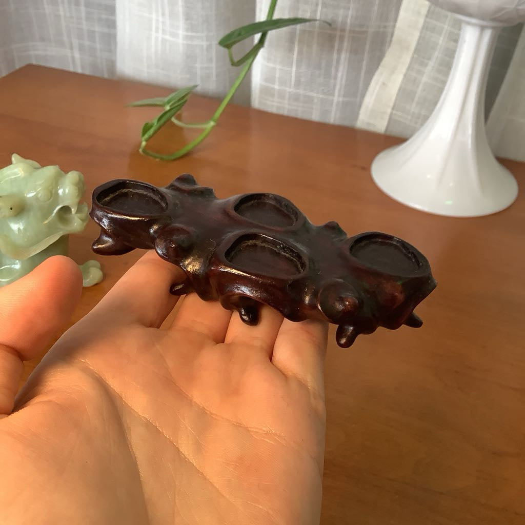 Hand holding a wooden knuckle duster with a plant and white candle holder in the background.