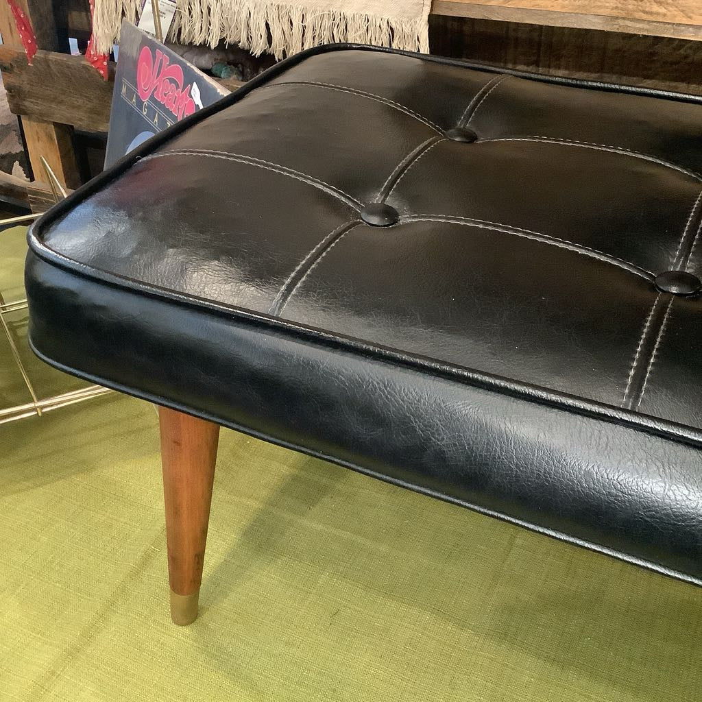 Black leather ottoman with wooden legs on a green floor