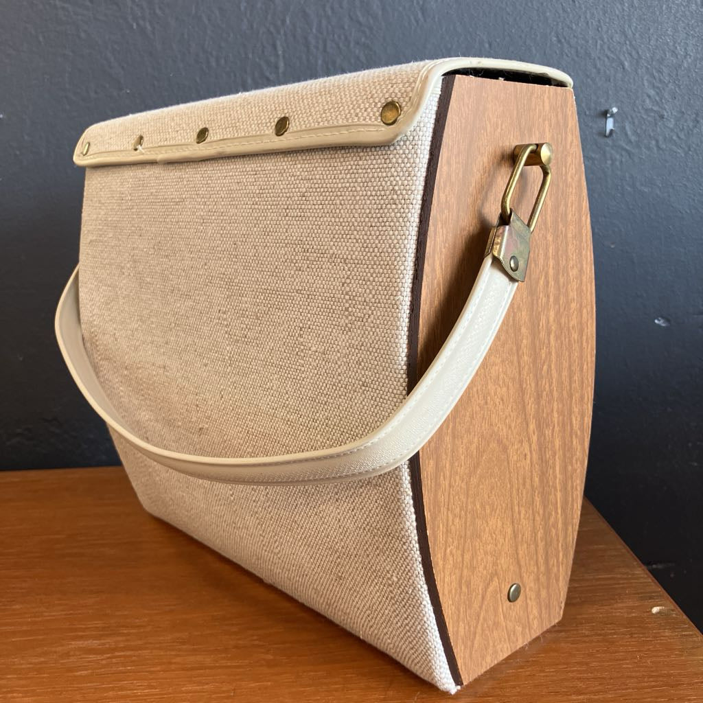 The back of a wooden and fabric handbag on a wooden surface and with a dark background.