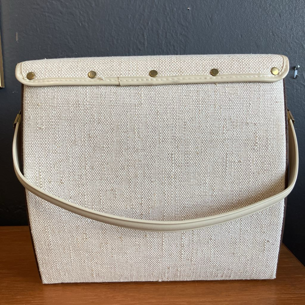 Beige textured handbag with a strap on a wooden surface against a dark wall.