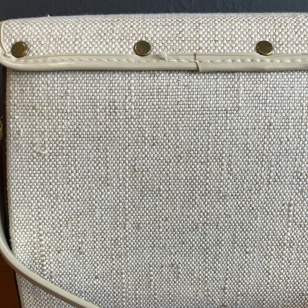 Close-up of a textured white clutch with gold studs on a dark background