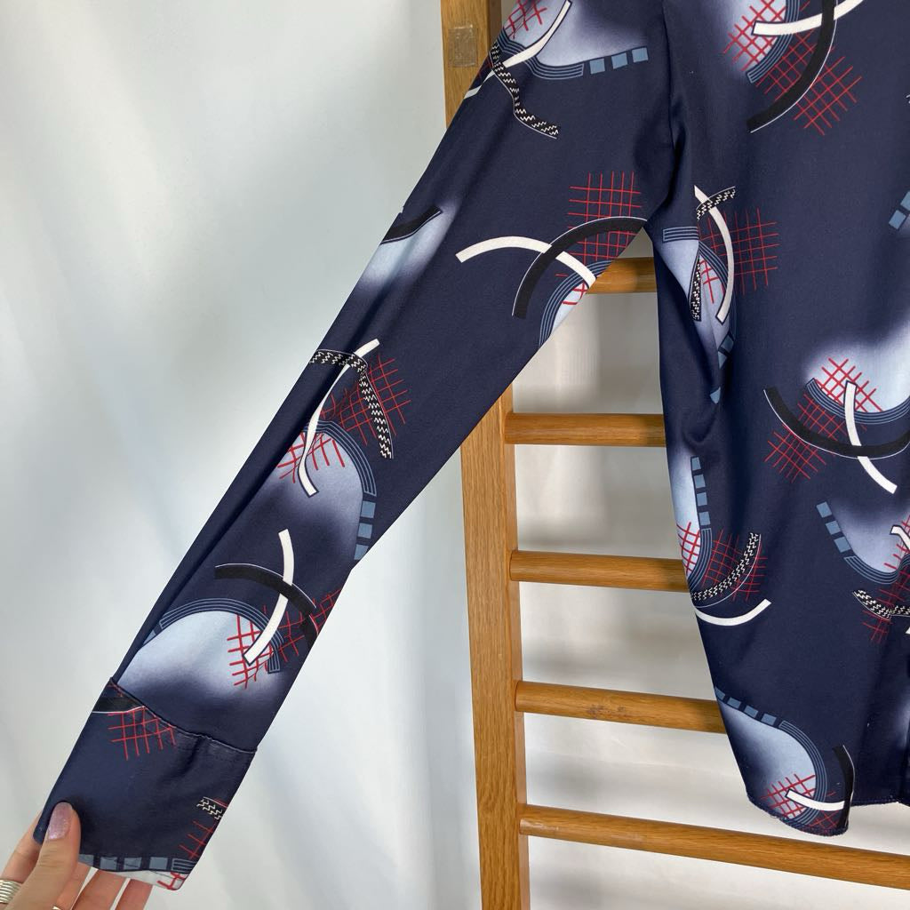 A navy blue long-sleeve top with a baseball-themed graphic print, draped over a wooden ladder. A hand is holding up the cuff of the sleeve to show the fabric detail.