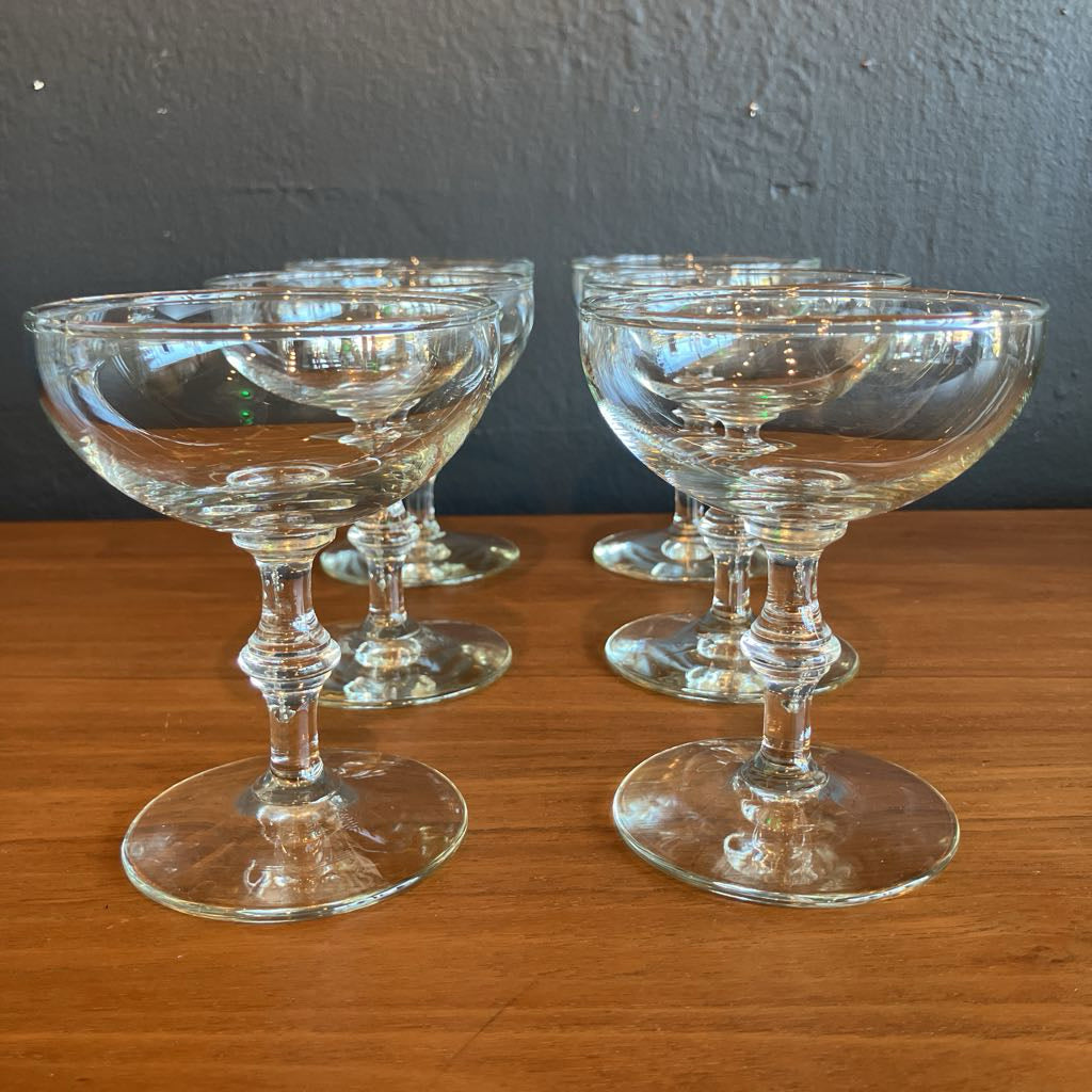 Set of six clear glass cocktail glasses on a wooden surface with a dark gray wall background.