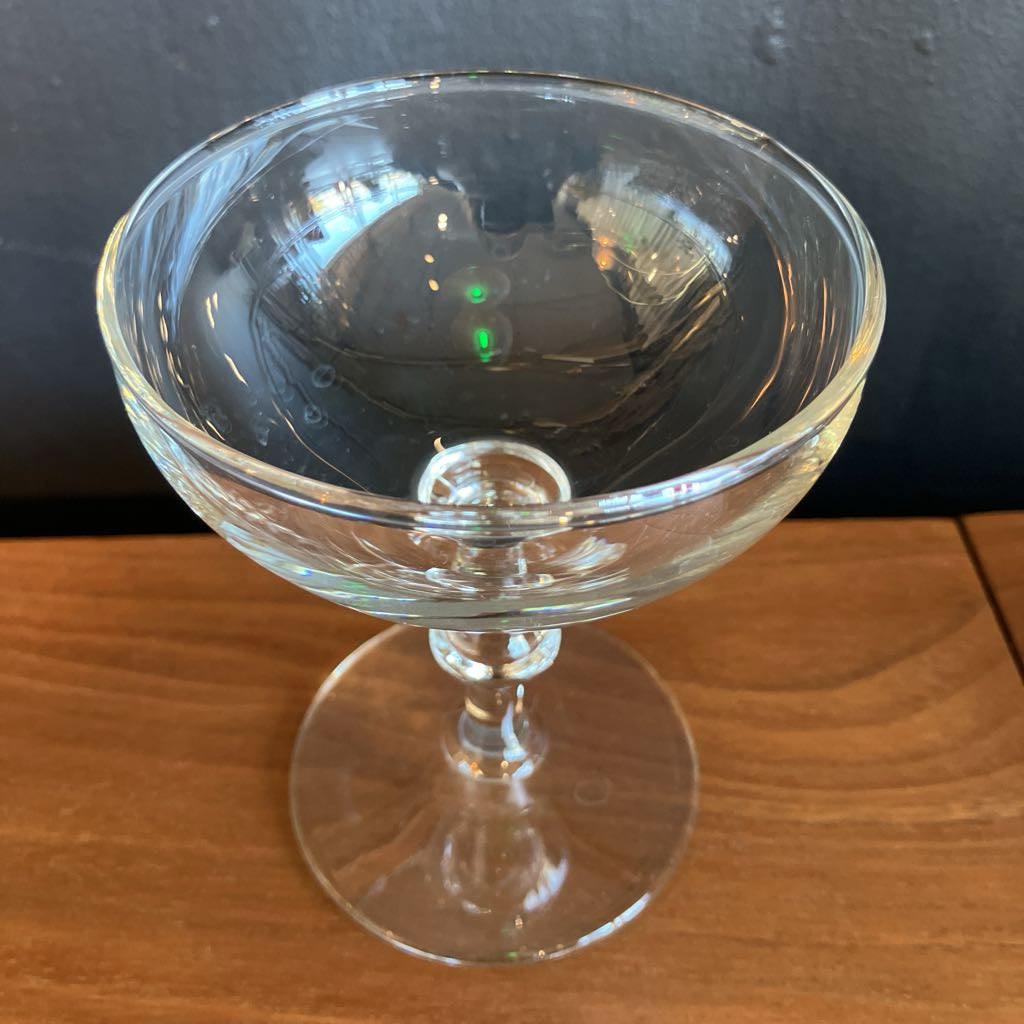 Clear glass coupe on a wooden surface with a dark background