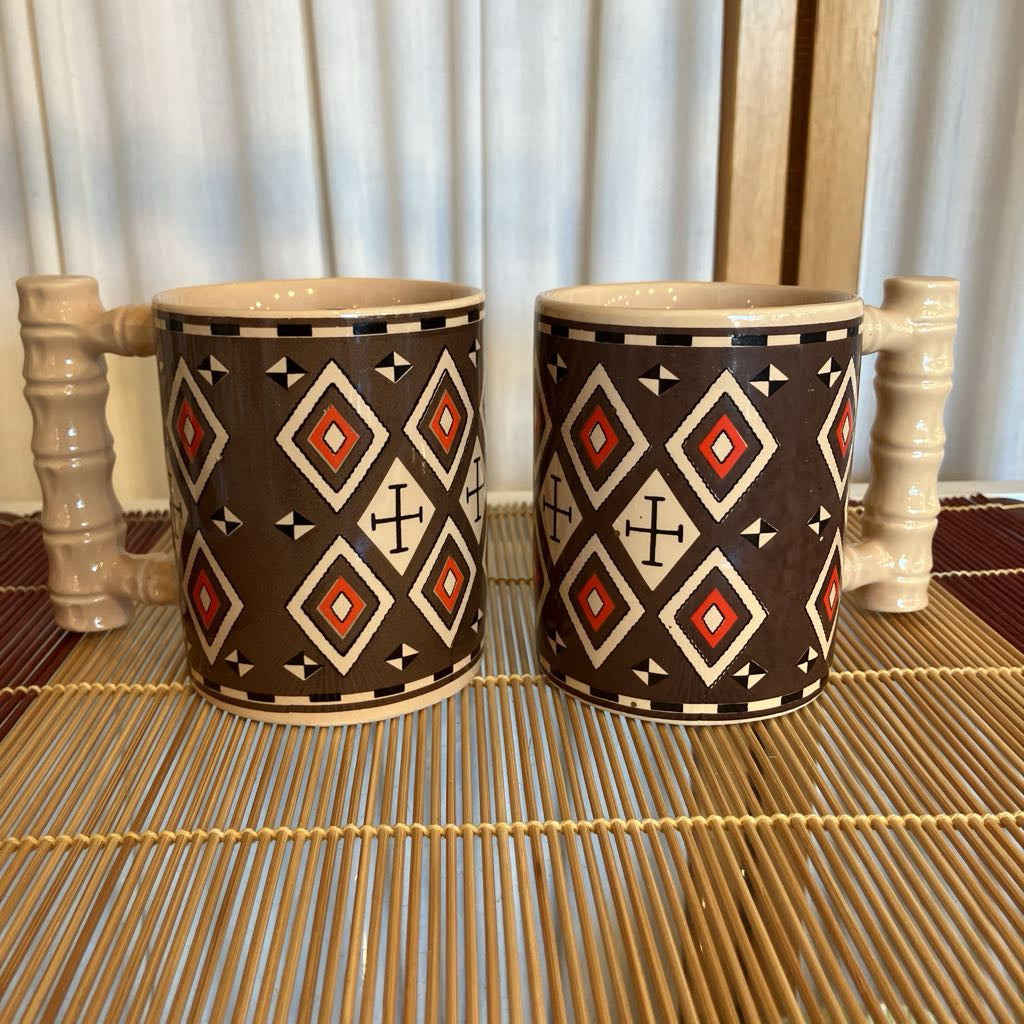 Two ceramic mugs with geometric patterns on a woven mat.