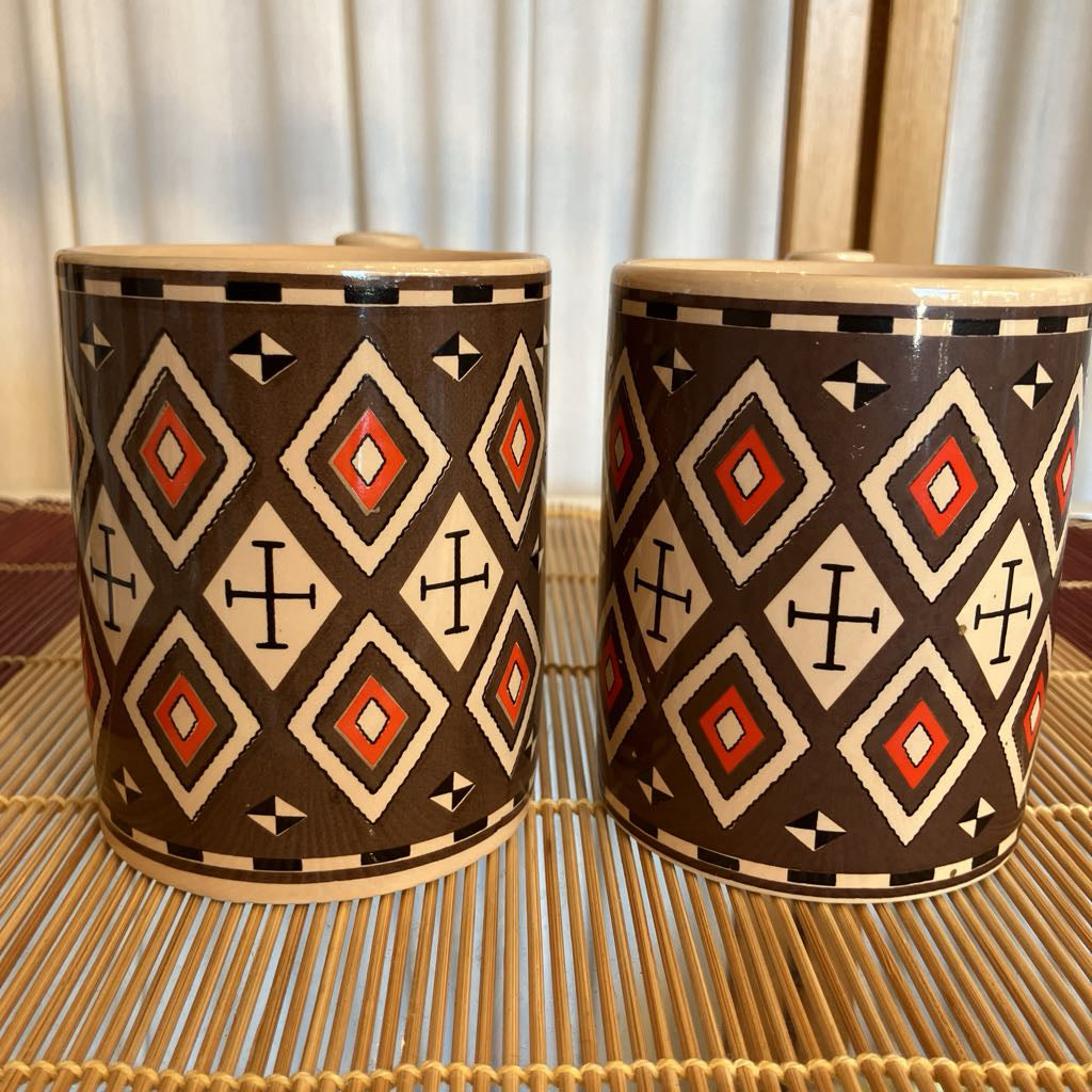 Two ceramic mugs with geometric patterns on a woven surface.