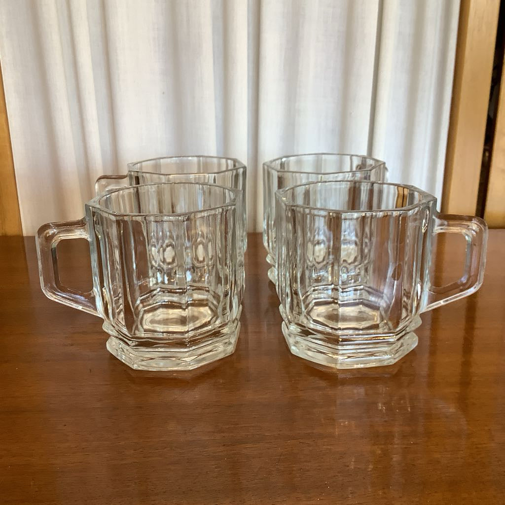 Set of five clear glass mugs with handles on a wooden surface.