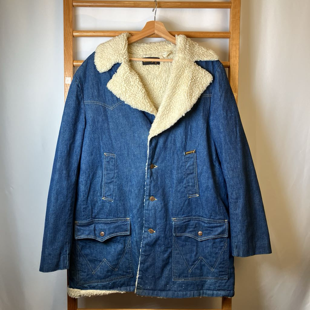 Blue denim jacket with cream sherpa lining on a wooden hanger against a neutral wall.