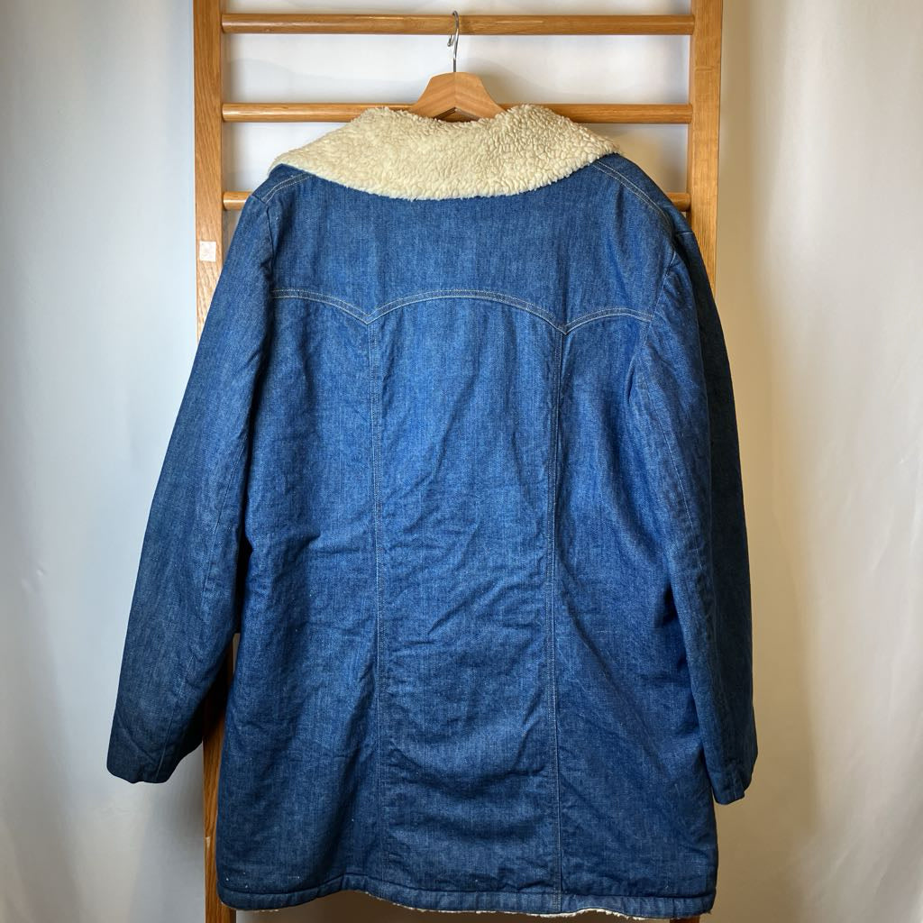 Blue denim jacket with cream collar on a wooden hanger against a white wall.