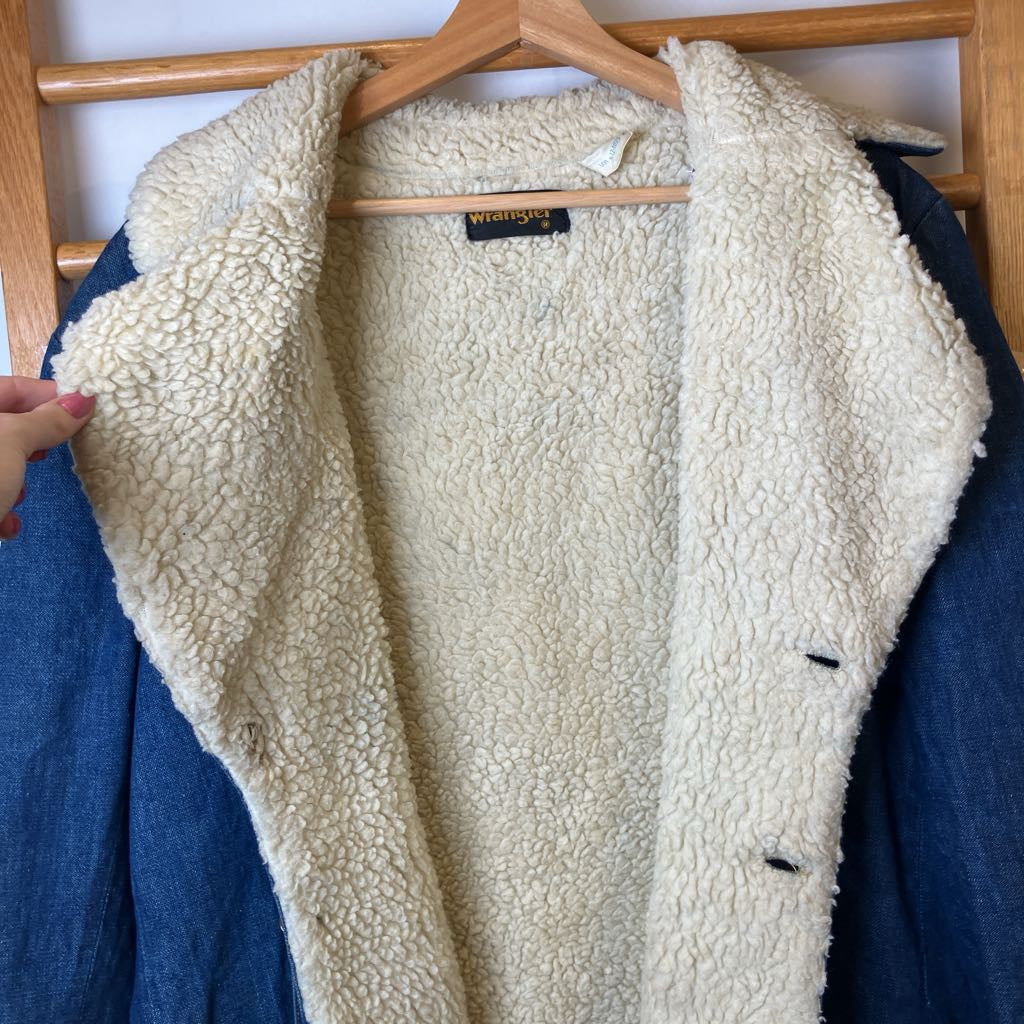 Beige sherpa-lined jacket on a hanger against a wooden rack.