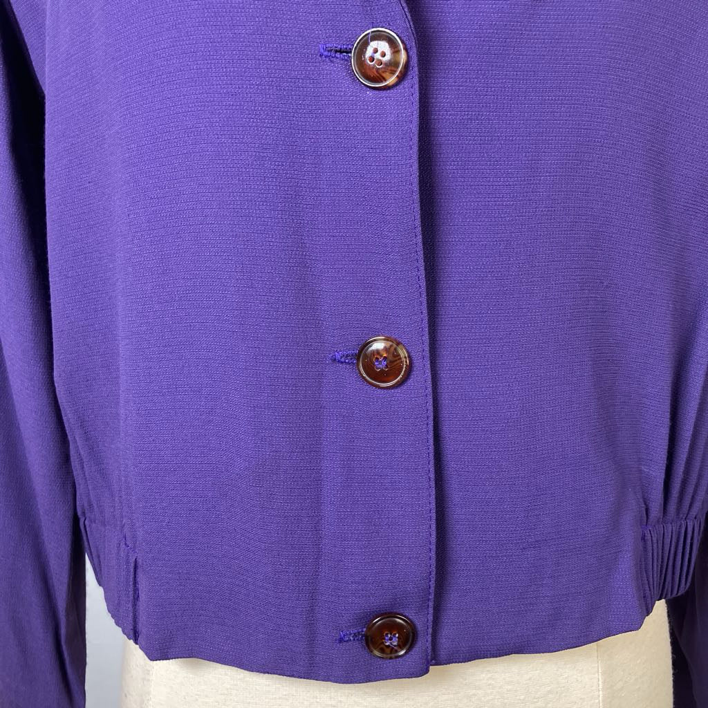 Close-up of a purple button-up garment with brown buttons on a white background