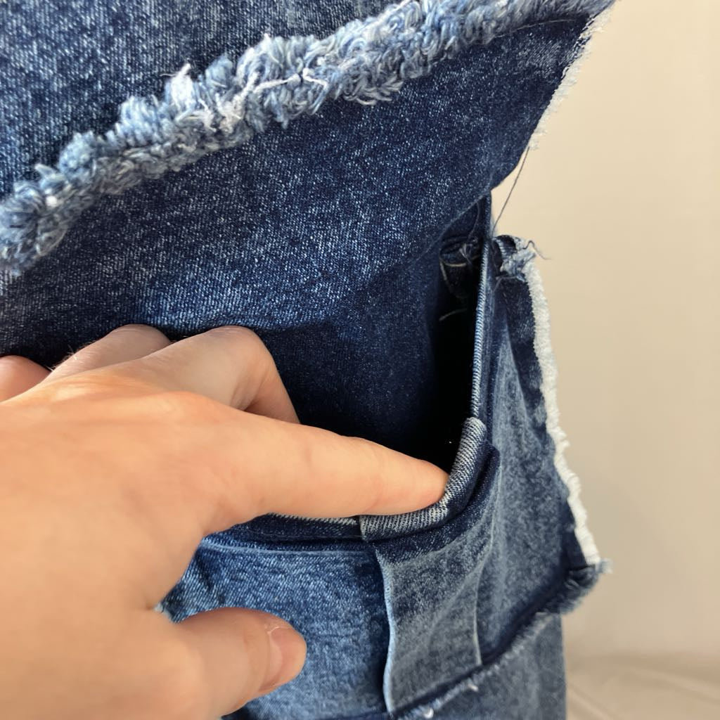 Close-up of a hand touching a blue denim fabric with frayed edges.