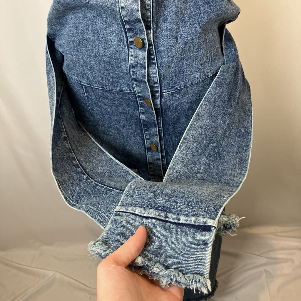Blue denim jacket with frayed hem held by a hand against a neutral background