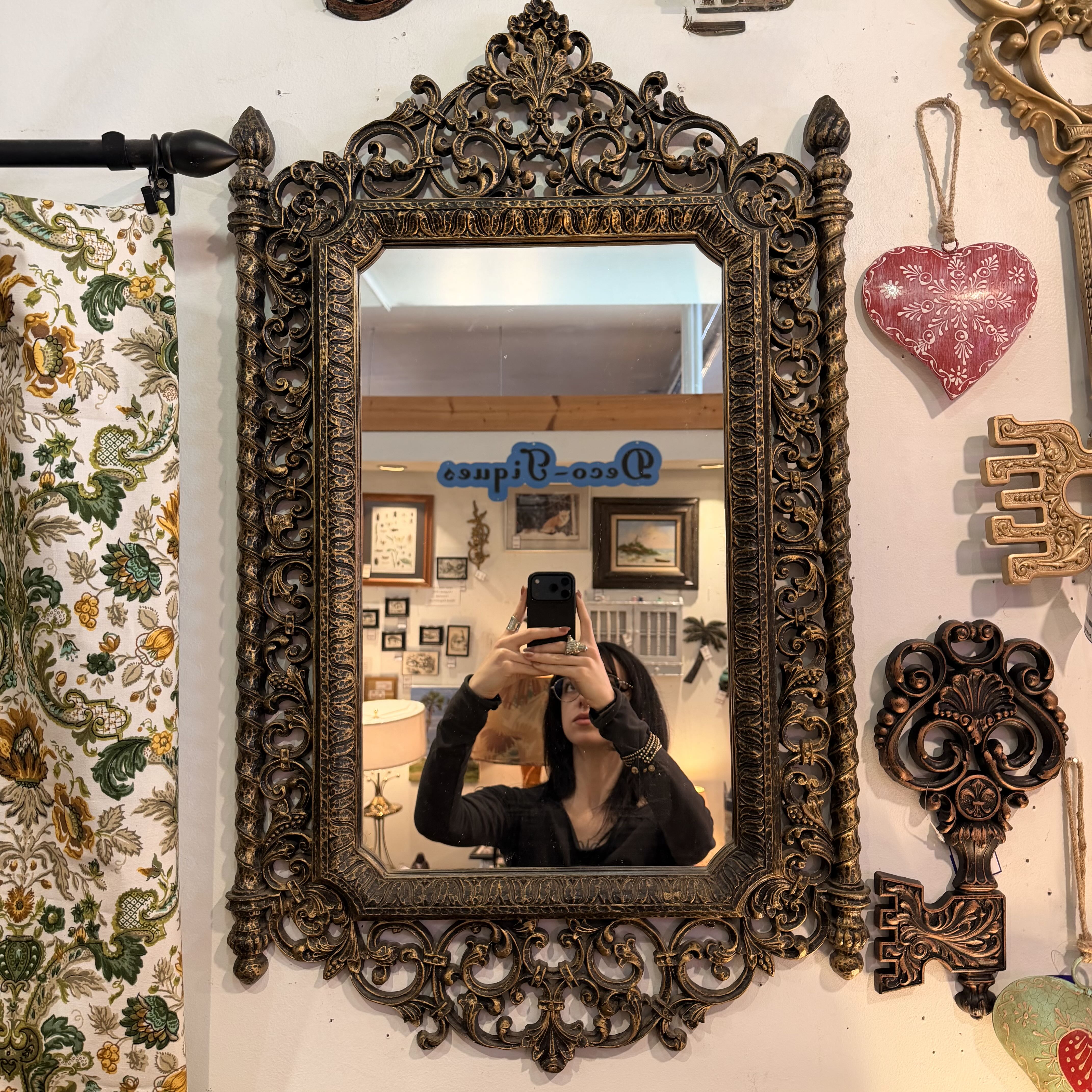 Decorative mirror with intricate gold frame on a wall with other decorative items.