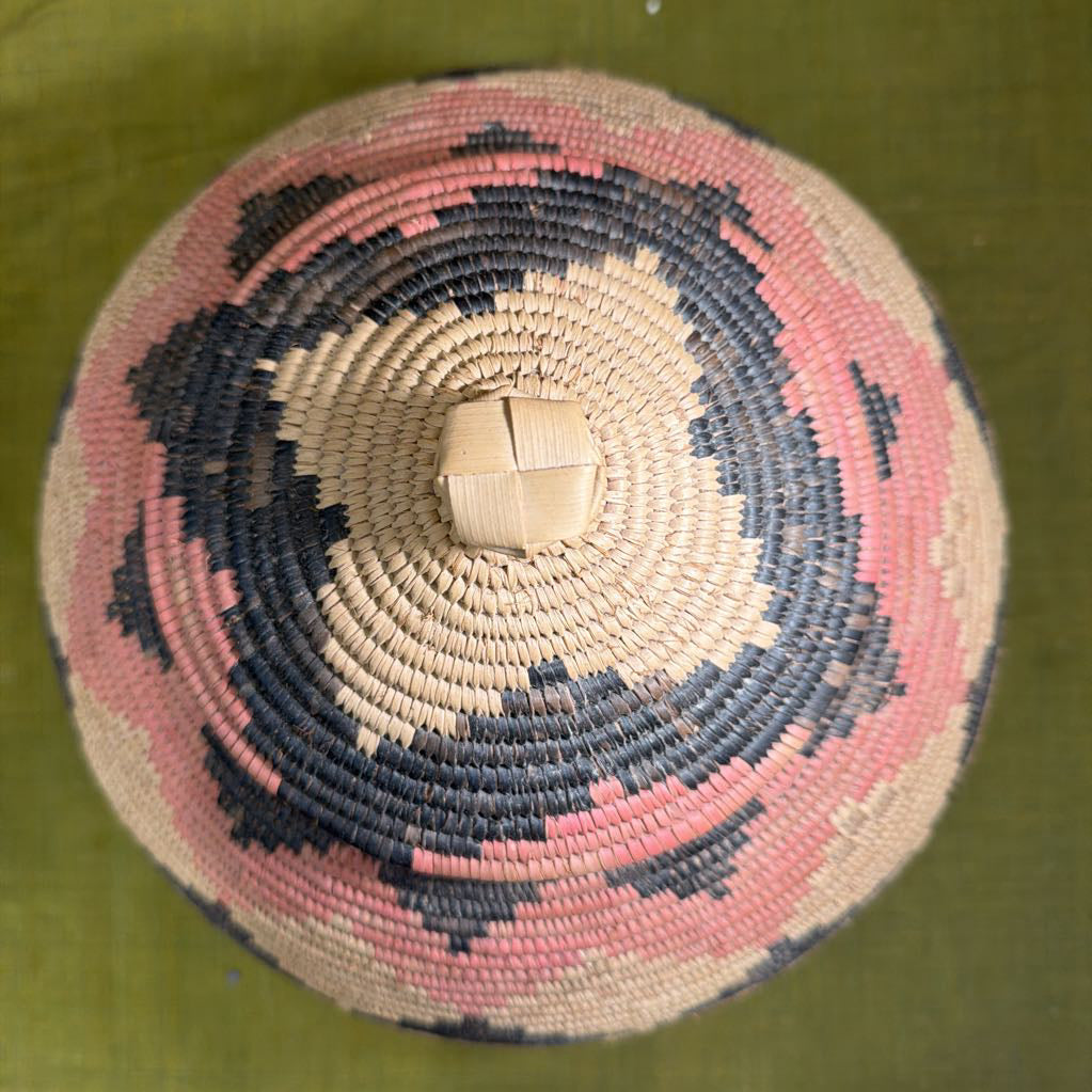 The top of a black, tan, and red patterned basket with a green background