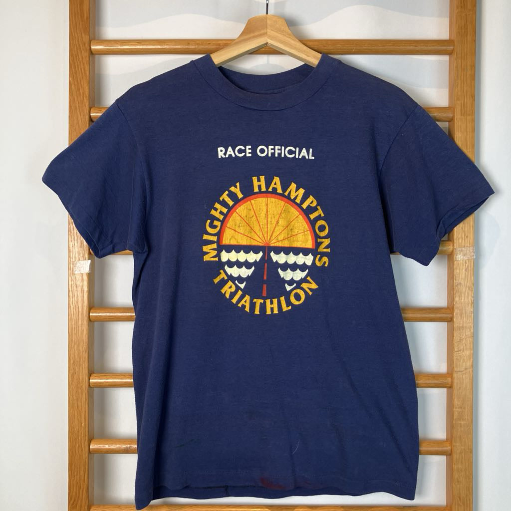 Navy blue t-shirt with 'Mighty Hamptons Triathlon' graphic on a wooden hanger.
