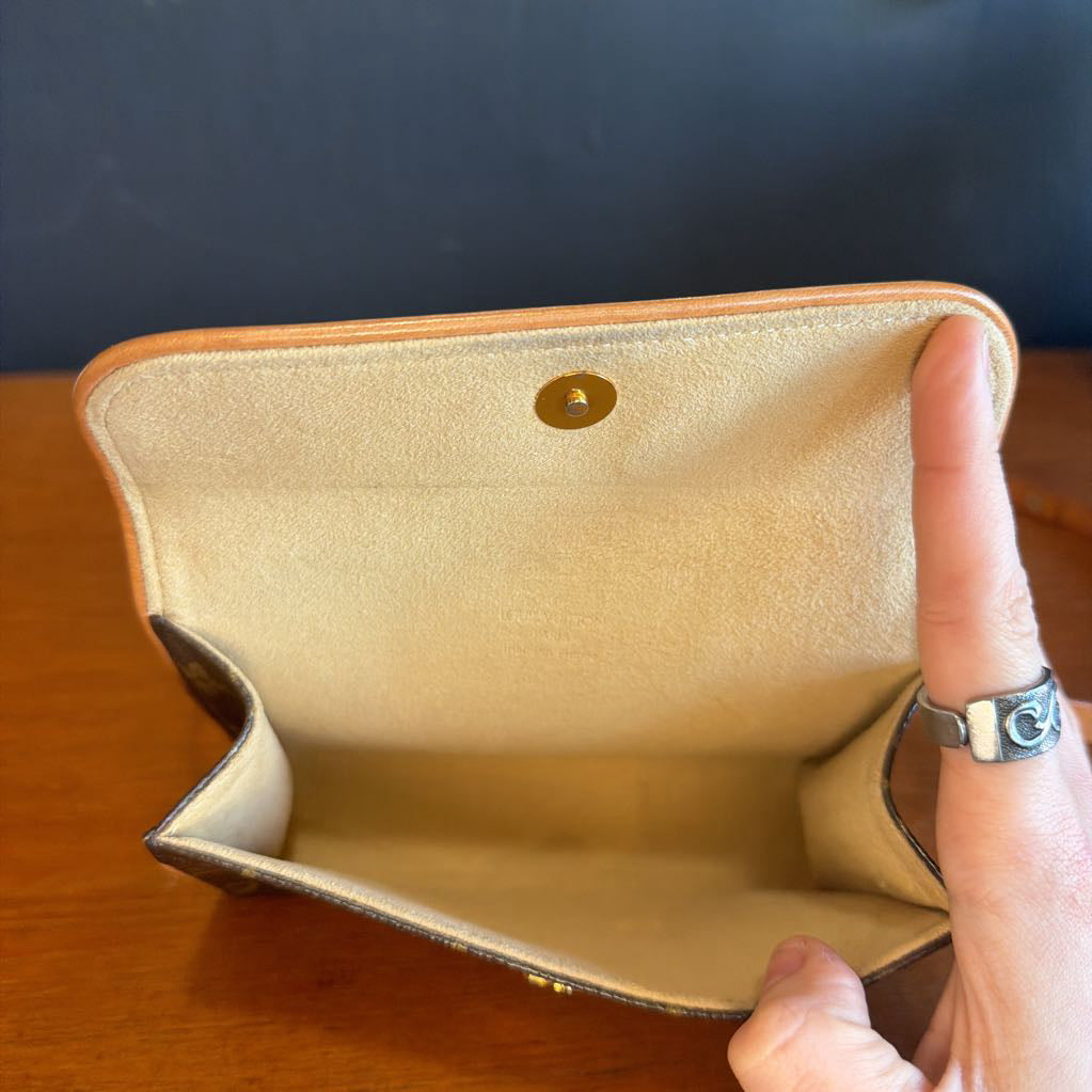 Beige handbag held by a hand with a ring on a wooden surface and dark background
