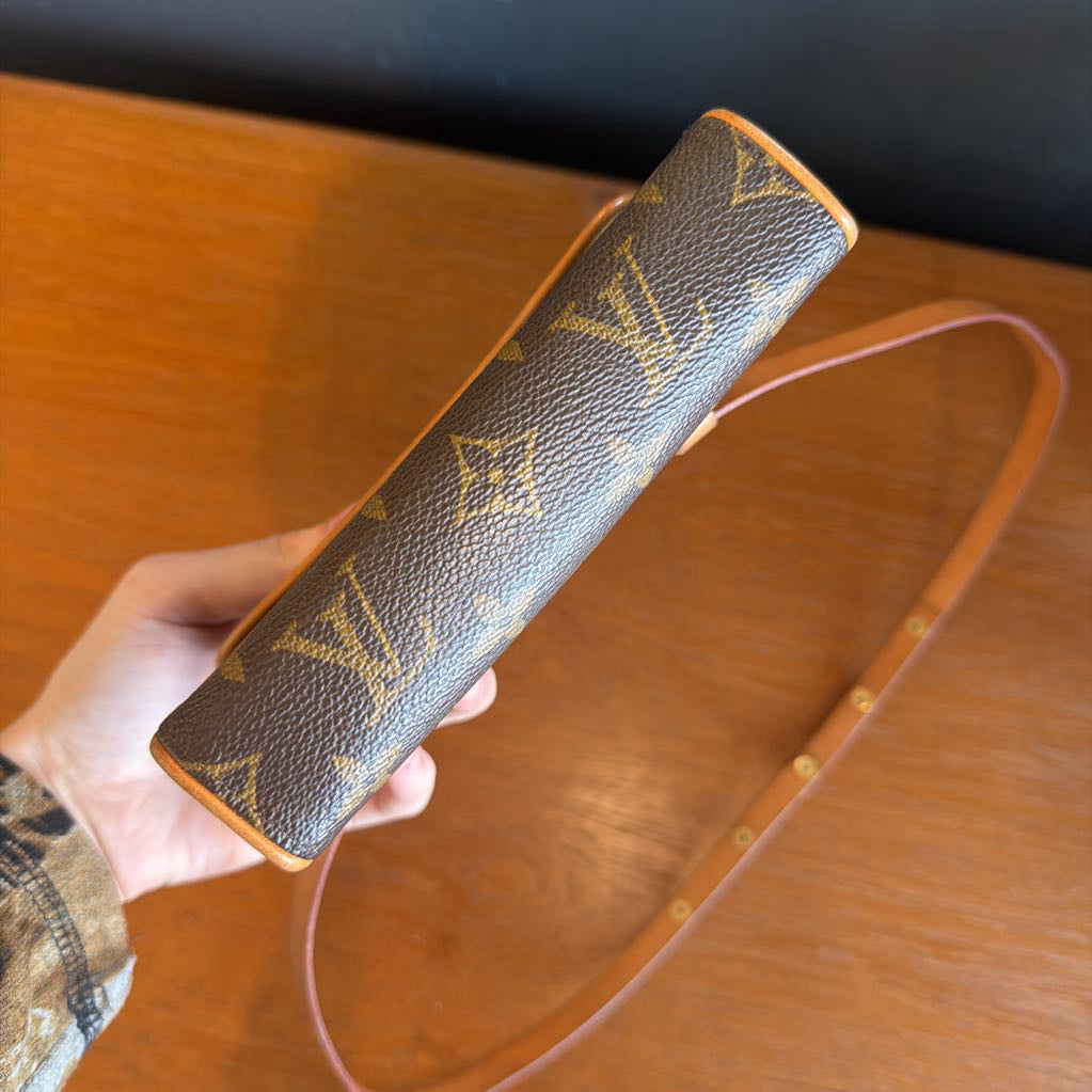 Louis Vuitton monogram belt with pink strap held by a hand on a wooden surface.