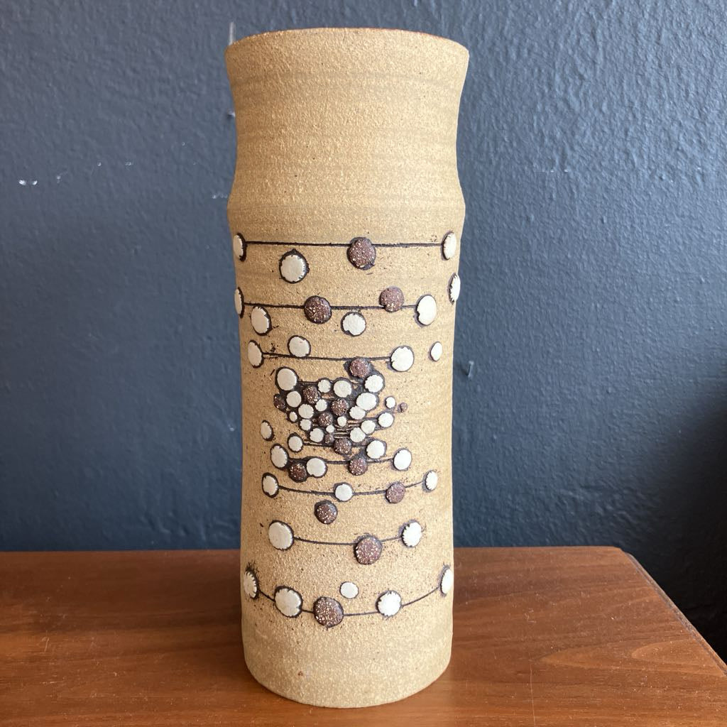 Beige ceramic vase with an abstract 3D dot design on a wooden surface and with a dark background.