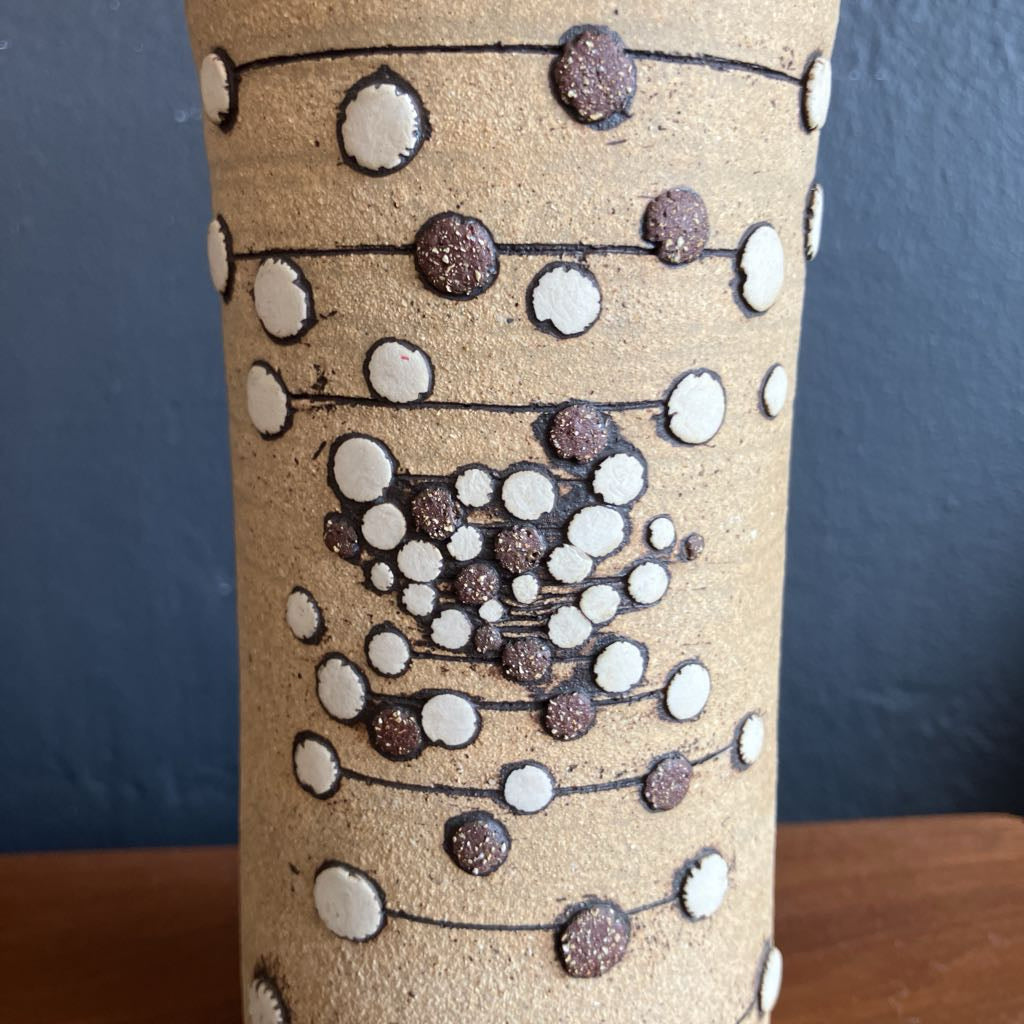 Beige ceramic vase with an abstract 3D dot design on a wooden surface and with a dark background.