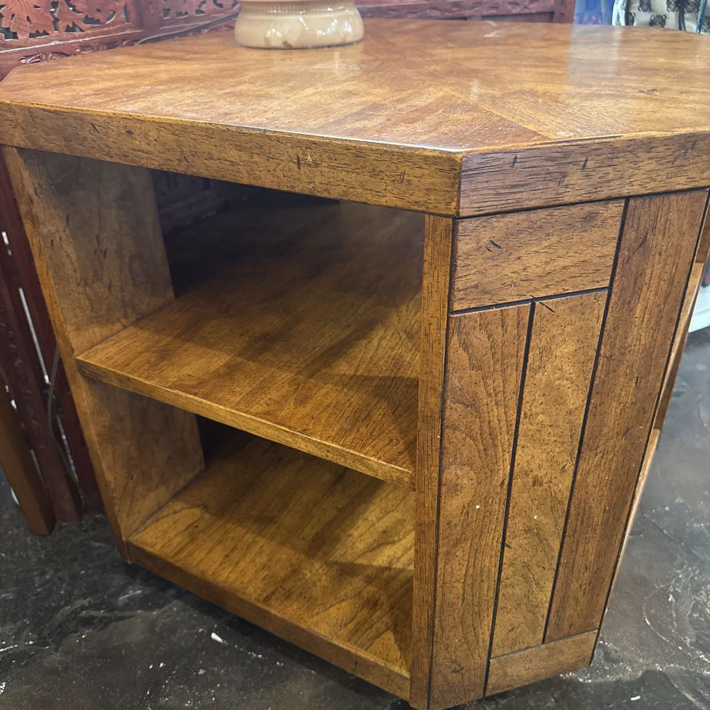 Brown wooden side table with shelves on a dark floor.