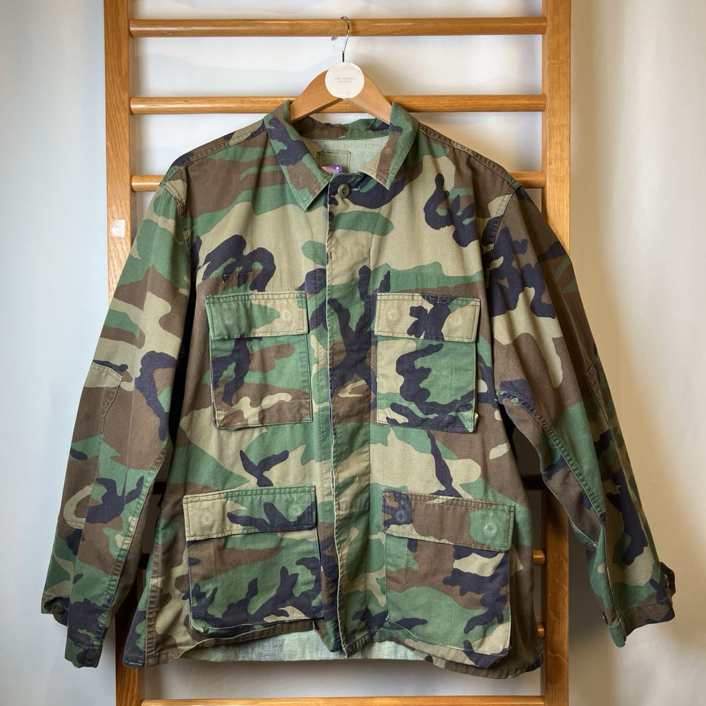 Camouflage jacket hanging on a wooden rack against a white wall