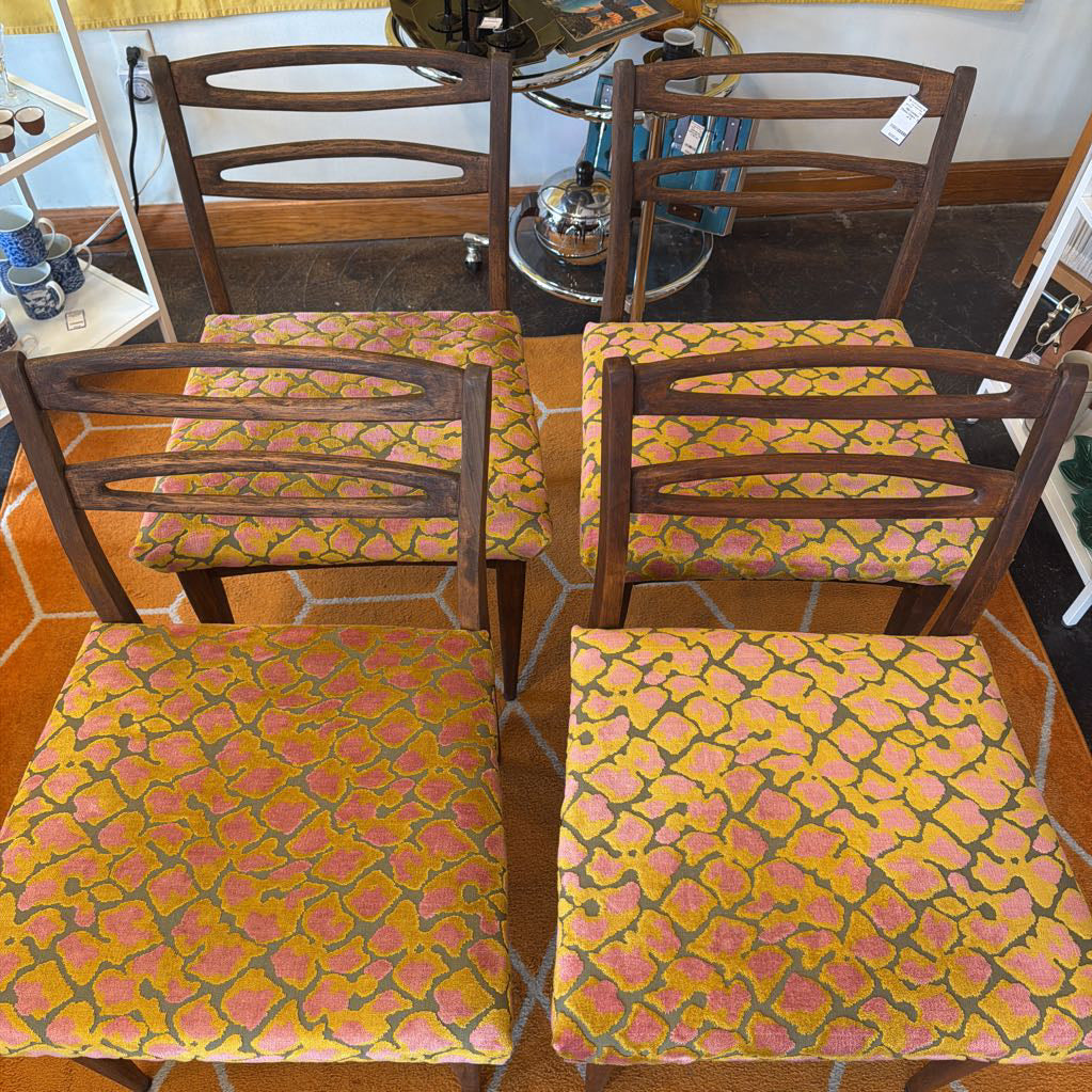 Four wooden chairs with patterned fabric seats in a room setting.