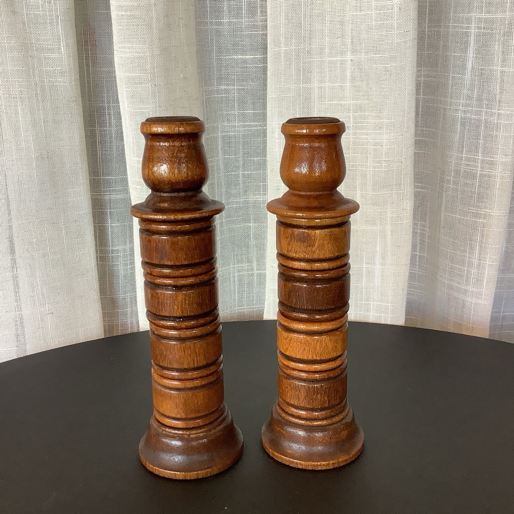 Two wooden candlesticks on a dark surface with a light curtain background