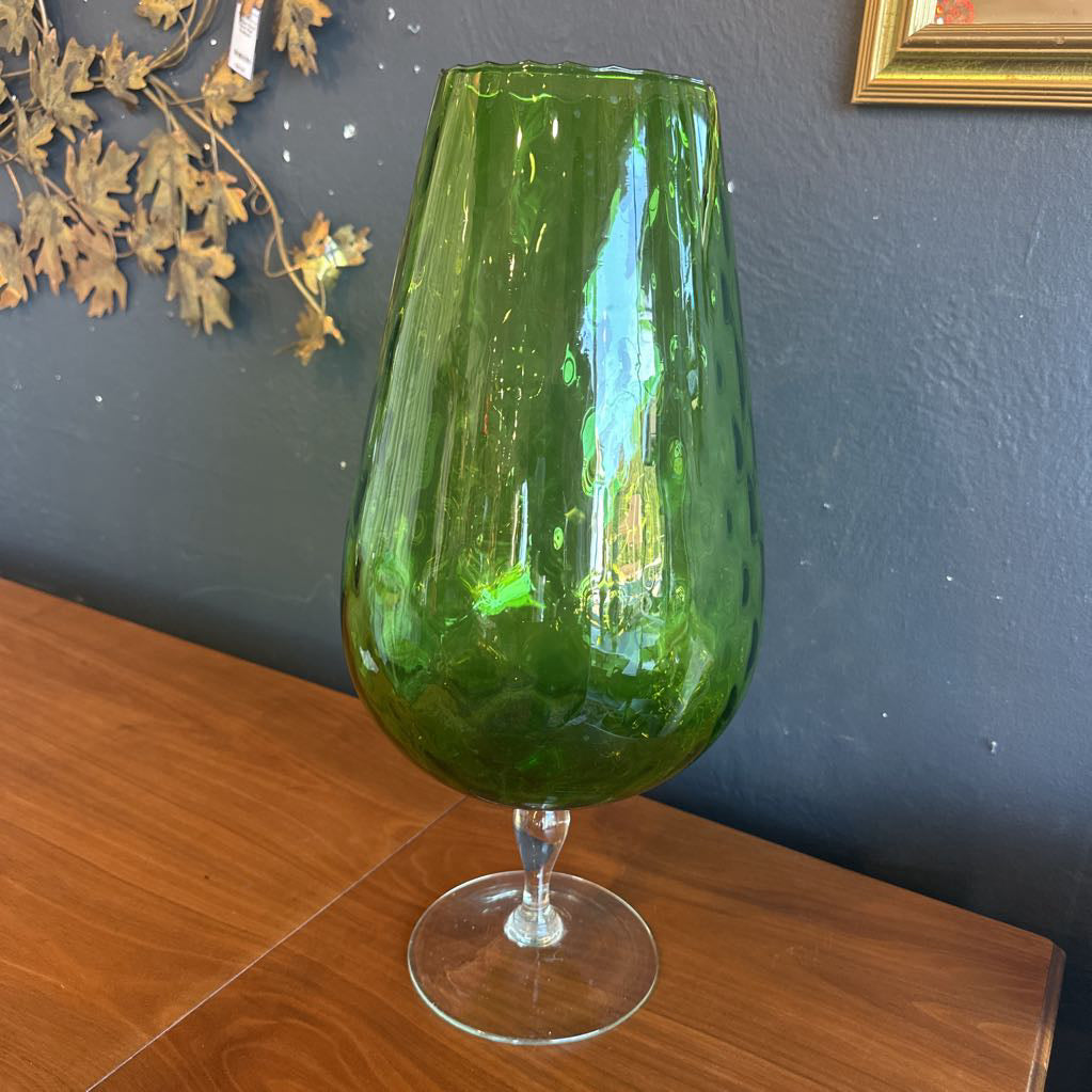 Green glass vase on a wooden surface with a dark wall background