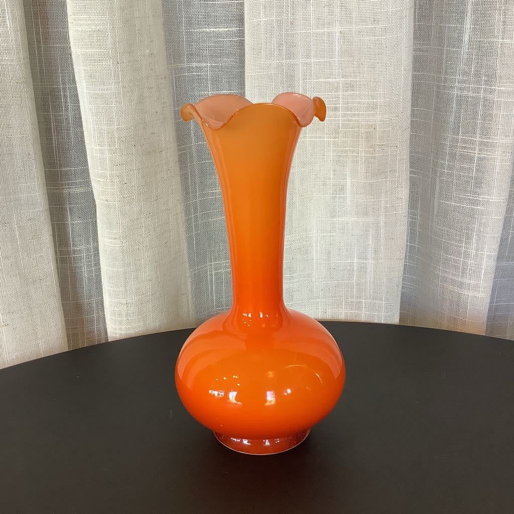 Orange glass vase on a dark surface with a light curtain background
