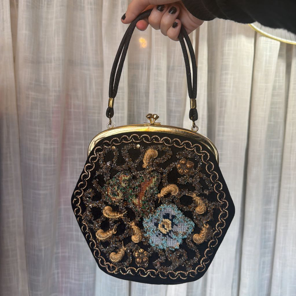 Decorative handbag with floral embroidery held by a hand against a neutral background