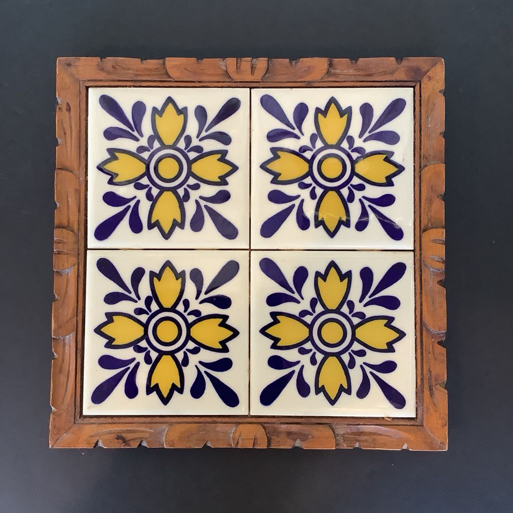 Decorative tile with floral design in purple and yellow, framed in wood against a dark background