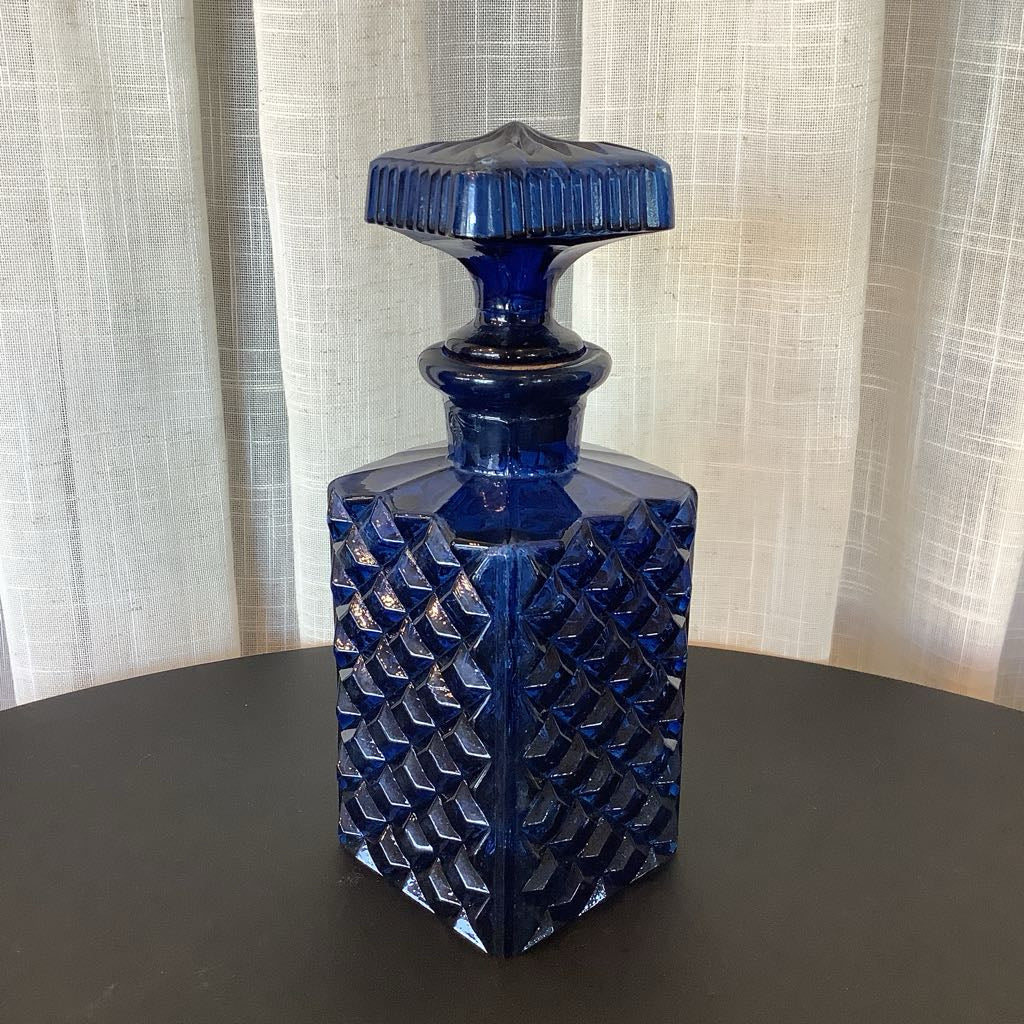 Blue glass decanter with diamond pattern on a dark surface