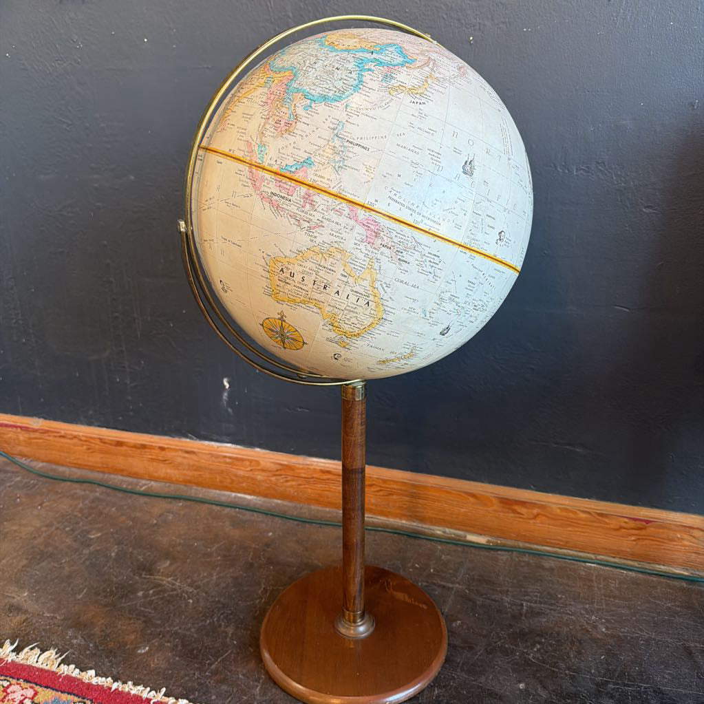 Vintage terrestrial globe on a stand against a dark wall.