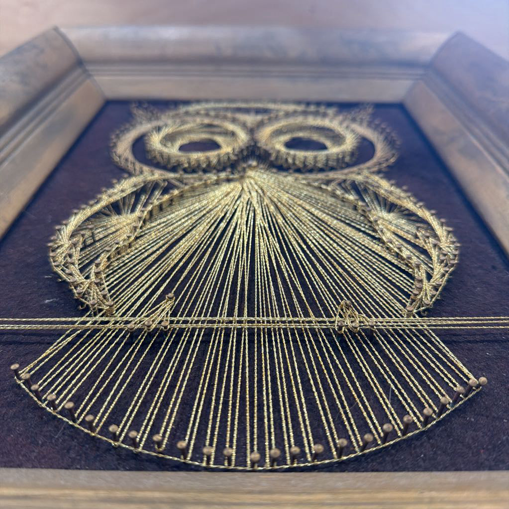 framed bronze owl string art against a dark brown fabric background