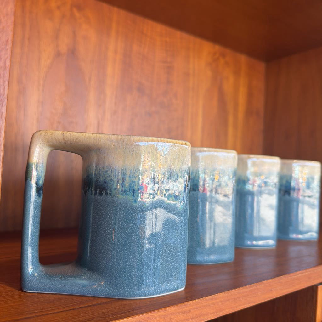 Row of blue ceramic mugs on a wooden shelf