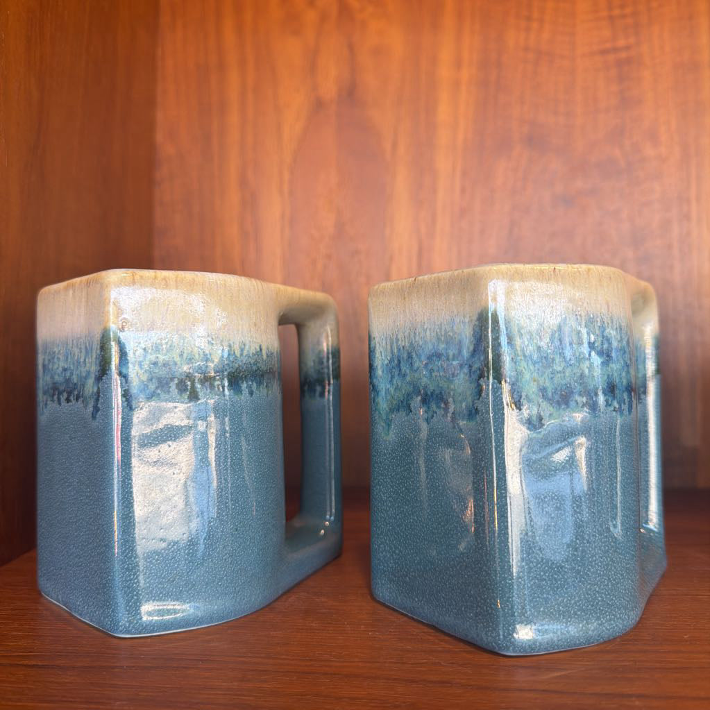 Two ceramic mugs with blue glaze on a wooden surface and background