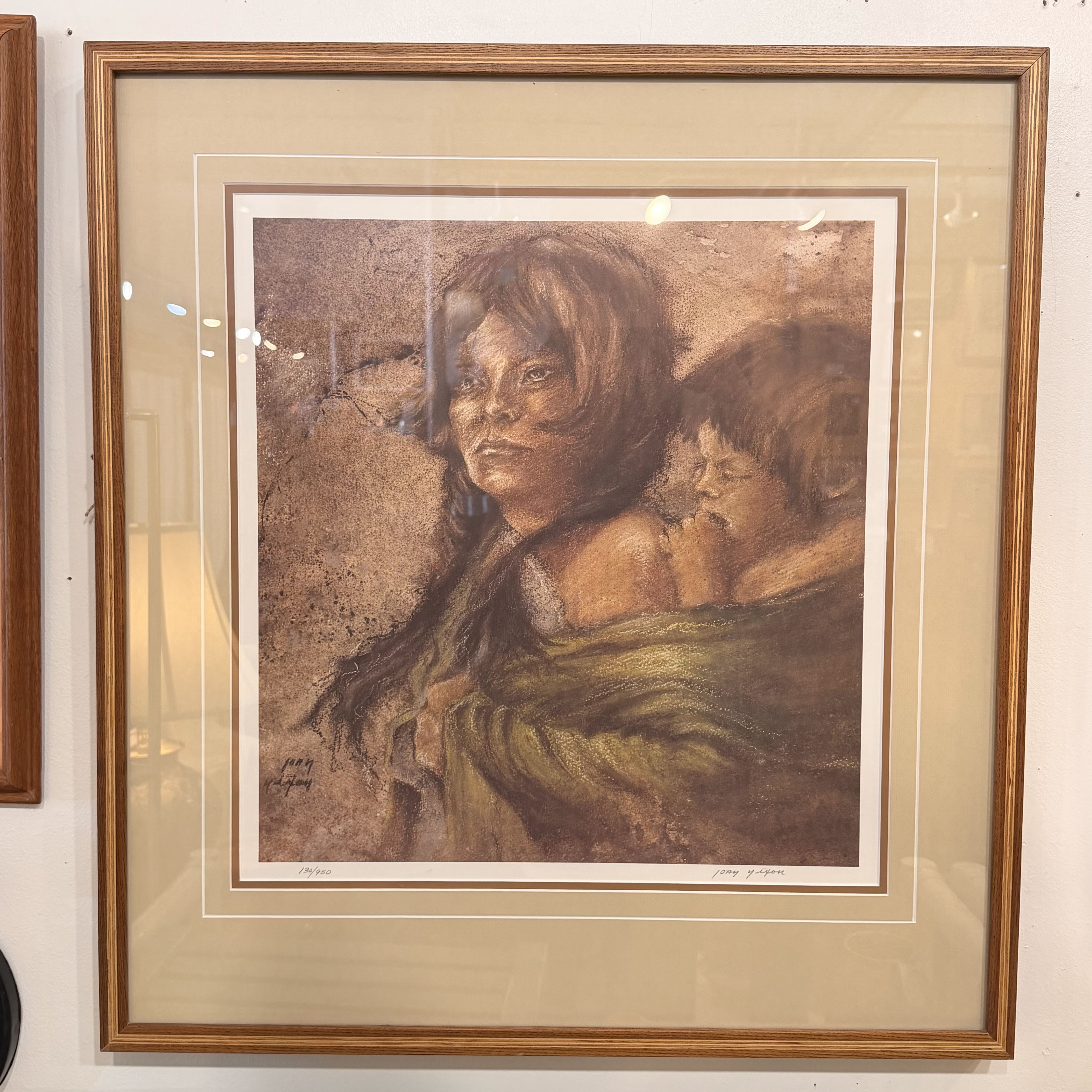 Framed artwork of a woman with a child on her back, displayed on a wall.