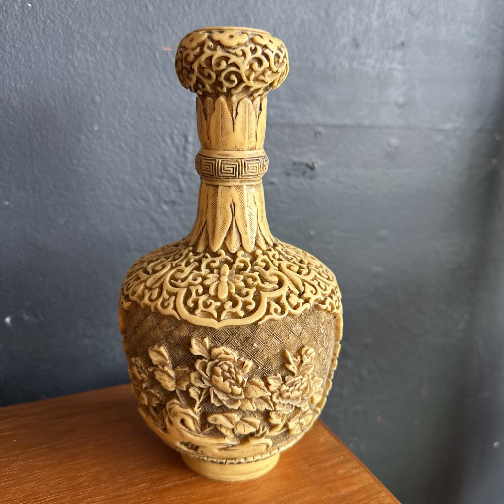 Decorative gold vase with intricate patterns on a wooden surface against a gray wall.
