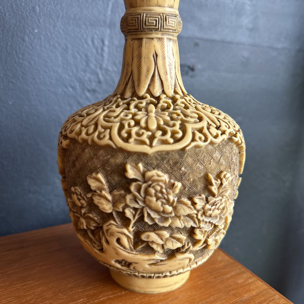 Decorative vase with intricate carvings on a wooden surface against a blue wall.